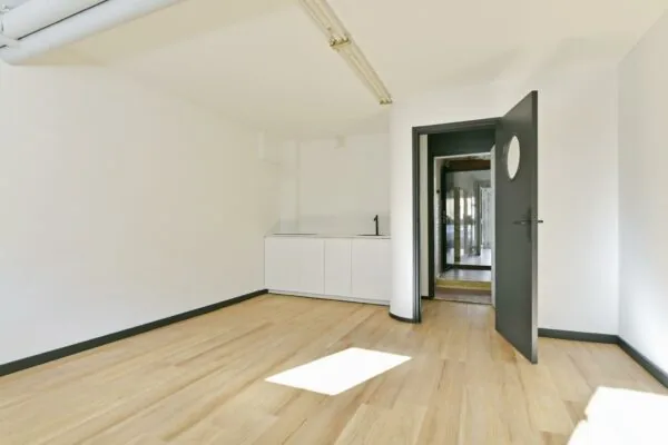 Licht en modern interieur van een lege kamer aan de Cornelis Dopperkade met houten vloer, wit keukenblok en zwarte deur.